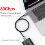 Dėmesio centre: 80 Gb/s duomenų perdavimo greitis Vaizdas: iš viršaus į apačią matomas kabelis, jungiantis nešiojamąjį kompiuterį su išoriniu standžiuoju disku / SSD. Pagrindinė informacija: Dideliame raudoname tekste rašoma 80 Gb/s ir teigiama, kad 15 GB failą galima perkelti per maždaug 1 sekundę.
